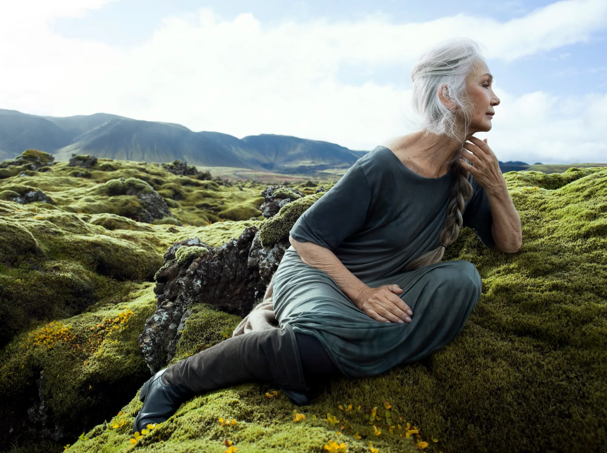 Silver-haired model seated on volcanic moss beneath open highland sky
