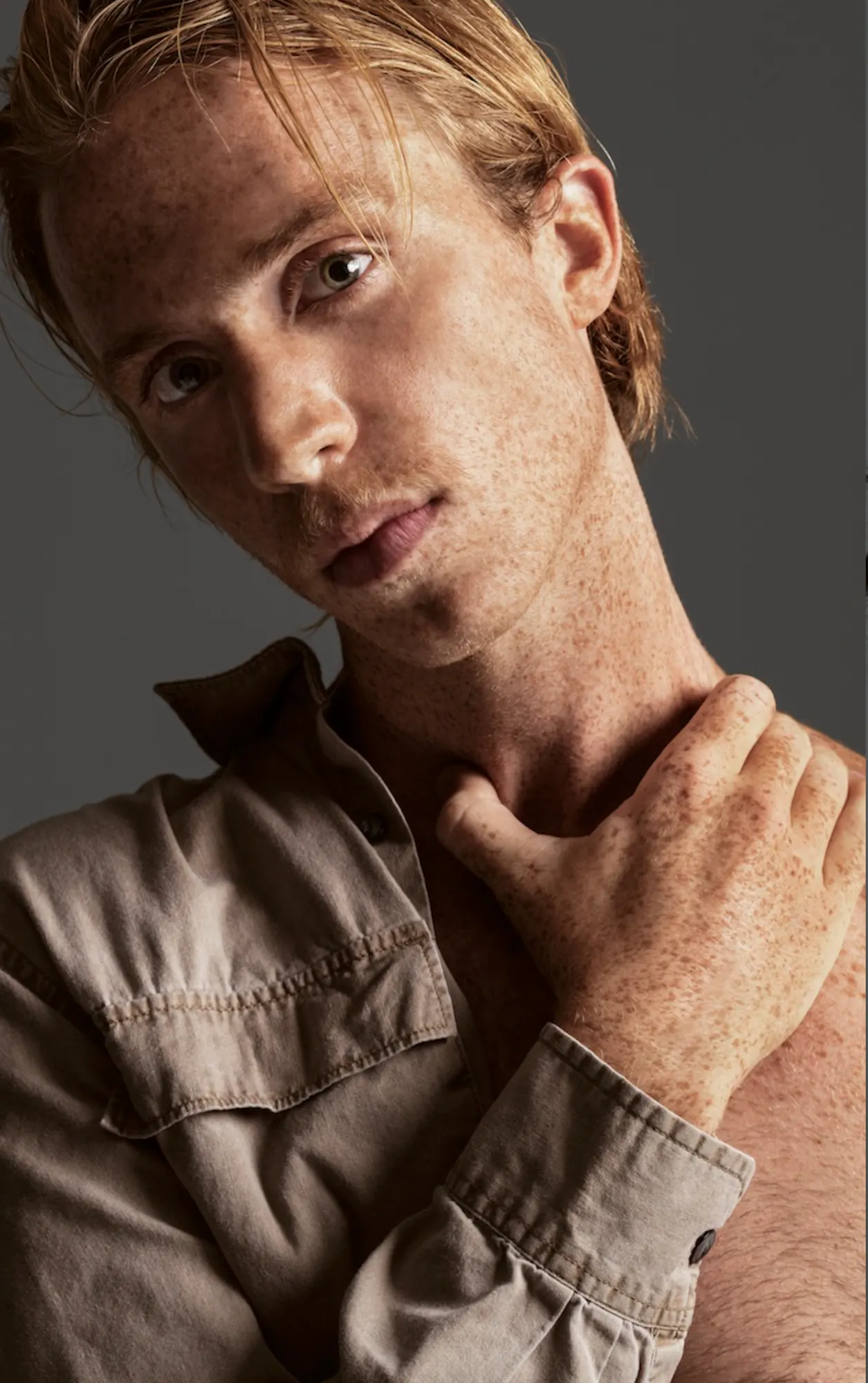 Close portrait of a freckled model with a hand at the collarbone